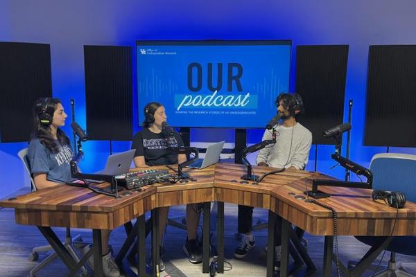 Undergraduate Research Ambassador's Sarisha Lohano and Hannah Allen interviewing UK undergraduate student Abdallah Sher on the OUR Podcast in a recording room in front of a blue screen depicting OUR Podcast logo