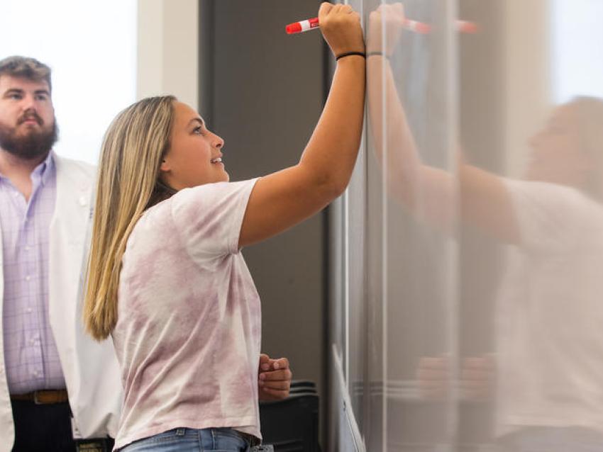 ACTION member and Lawrence County high schooler Kassidy Burke writes on a white board during a lecture given by ACTION alumnus and current medical student Scotty Farmer.